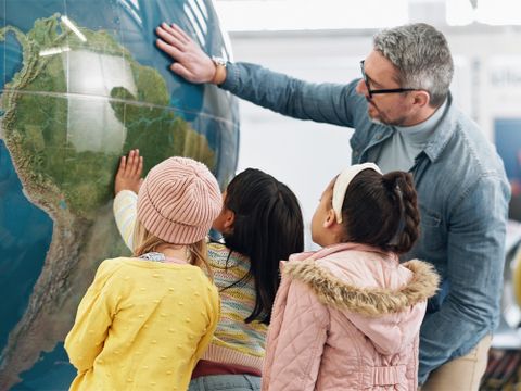 Lehrer steht mit Schülerinnen vor großen Globus