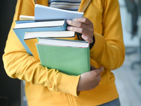 Mädchen hält einen Stampel Bücher in ihren Arrmen - Fotoausschnitt vom Oberkörper