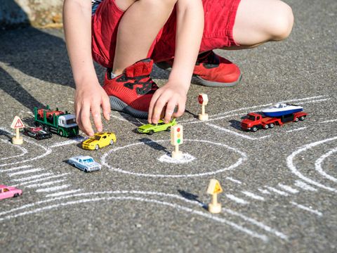 Junge spielt mit Modellautos auf einer Straße, dort ist mit Kreide ein Kreisverkehr aufgemalt