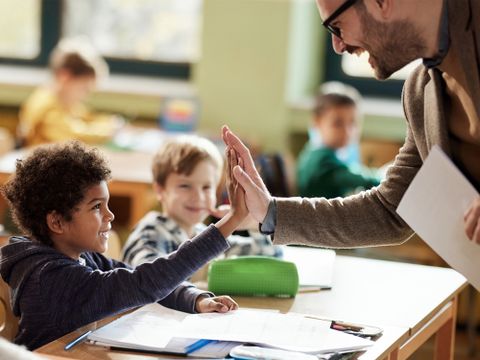 Freudiger Lehrer gibt jungem Schüler im Klassenraum High-Five