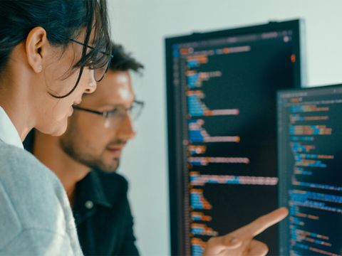 Zwei Menschen sitzen vor einem Computer und codieren