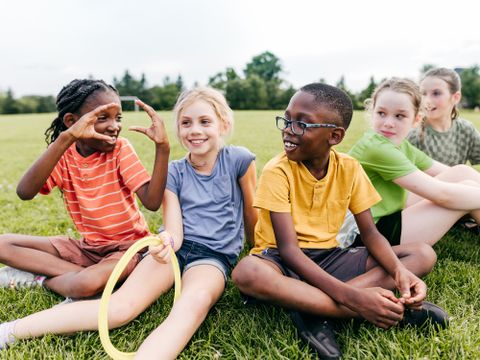 Mehrere Kinder sitzen auf einer Wiese und erzählen sich etwas