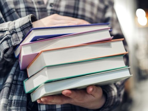 Mädchen hält einen Stampel Bücher vor ihrem Bauch - Bildausschnitt vom Oberkörper