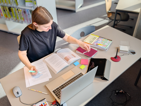 junger Mann sitzt mit Arbeitsmaterialien im Medienforum an einem Schreibtisch
