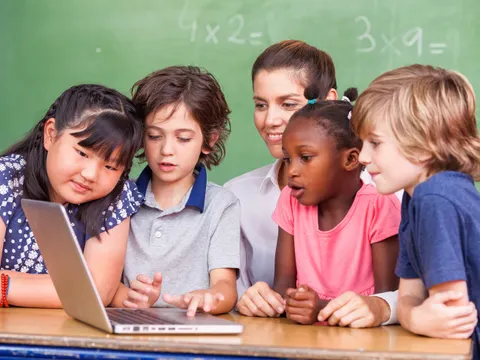 Schülerinnen und Schüler sitzen mit Lehrerin vorm Laptop