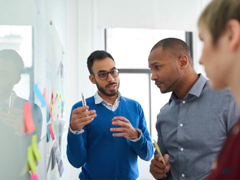 Erwachsene stehen vor einem Whiteboard und diskutieren