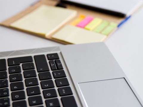 Laptop und Klebezettel liegen nebeneinander auf einem Schreibtisch