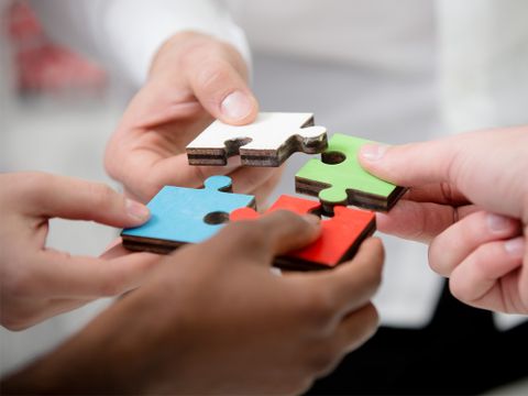 Mehrere Menschen halten Puzzleteile in einem Kreis zusammen - Bildausschnitt auf die Hände