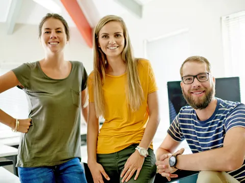 Zwei junge Frauen und ein Mann lächeln in die Kamera