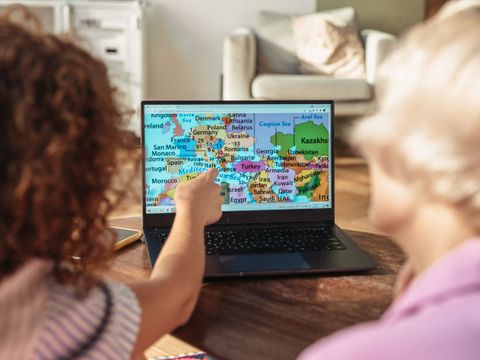 Kind sitzt mit Lehrerein vor dem Laptop, Länderkunde