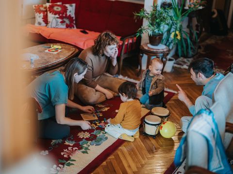 Erwachsene spielen mit Kleinkindern auf Boden in Wohnzimmer