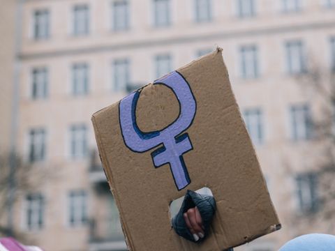 Eine Person hält ein Pappschild mit dem Frauenzeichen hoch.