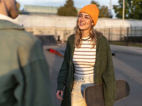 Junge Frau steht in Skatepark mit einem Skateboard und unterhält sich