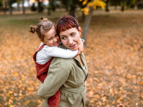 Verspielte Mutter und Tochter machen im Park ein Huckepack-Spiel