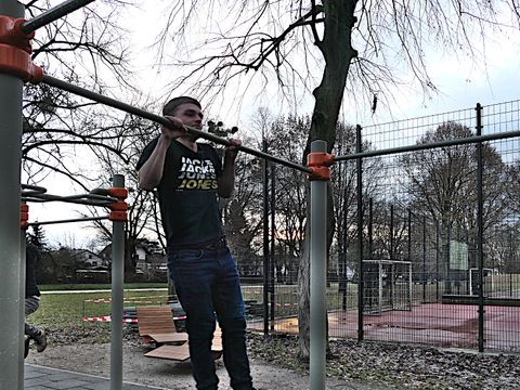 Junger Mann macht Klimmzug an Reckstange der Anlage