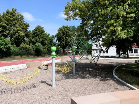 Spielfläche mit Hängematten und Kletterspinne, Sprintbahn auf baumbestandenen Schulhof