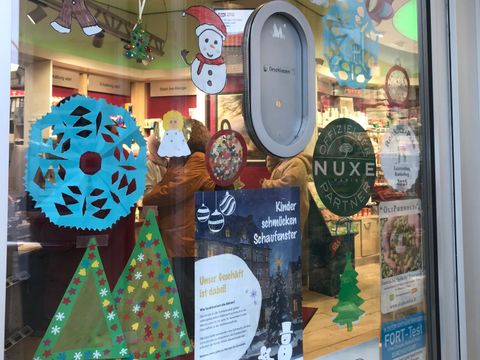 Gebastelter Weihnachtsschmuck an Scheibe und Plakat: Kinder schmüclen Schaufenster