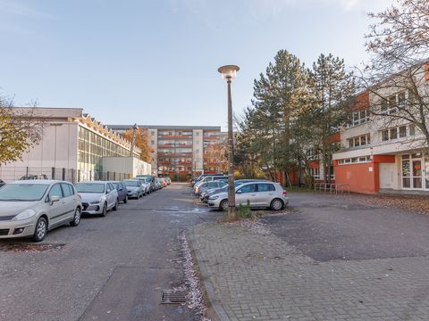 Schmale, zugeparkte Straße mit Kita und Sporthalle sowie querstehenden Plattenbau als Abschluss