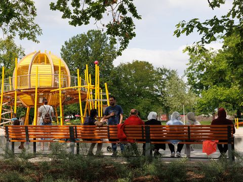 Bank vor der Spiellandschaft „Sterne und Galaxien". Die Eltern und Großeltern beobachten entspannt die Kinder beim Spielen.