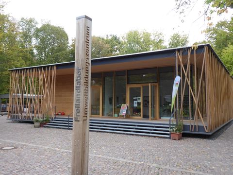 Das Freilandlabor Britz befindet sich in einem einstöckigen, modernen Gebäude mit Pultdach. Einige Stufen führen zu einer überdachten Terrasse, der Eingangsbereich ist großflächig verglast. Der überwiegende weitere Teil des Gebäudes ist mit Holz verkleidet. Auf dem gepflasterten Platz davor steht ein Holzpfahl mit den Schriftzügen „Freilandlabor“ und „Umweltbildungszentrum“. Im Hintergrund ragen Bäume auf.