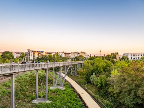 Fußgängerbrücke mit Menschen und Fahrrädern, darunter Bahnlinie, im Hintergrund Häuser und Berliner Fernsehturm.