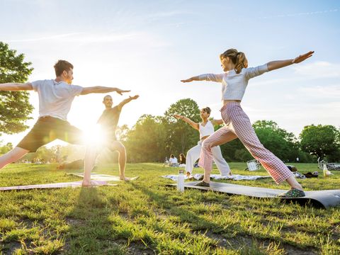 Menschen auf einer Wiese machen gemeinsam Yogaübungen bei Sonnenlicht.