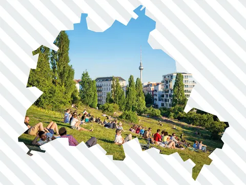 Menschen sitzen auf einer Wiese im Mauerpark mit Bäumen und Gebäuden im Hintergrund, ausgeschnitten in Form der Berliner Landkarte.