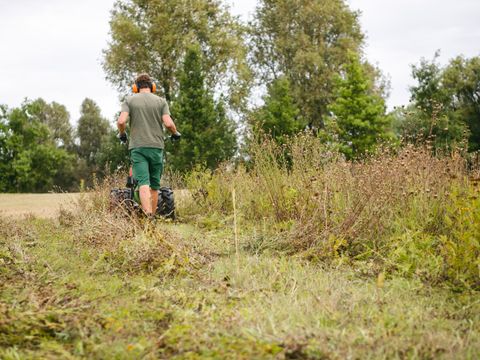 Ein Mann bei der Wiesenmahd. Der Mann trägt einen Gehörschutz.