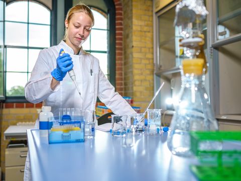 Eine Laborantin füllt ein reagenzglas mit einer Pipette