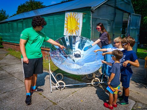 Zwei Erwachsene und drei Kinder an einem Parabolspiegel