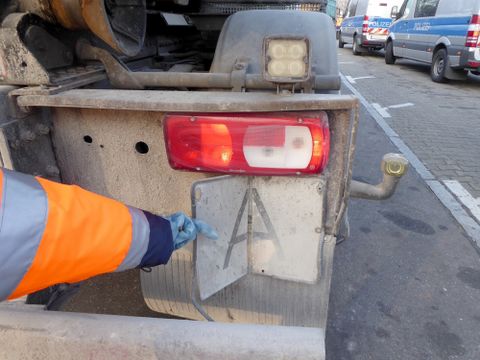 Ein Arm in Warnjacke hält ein Schild an das Heck eines Fahrzeugs, auf dem ein „A“ zu sehen ist. Dies zeigt an, dass in dem Fahrzeug Abfälle nach deutschem Recht transportiert werden.