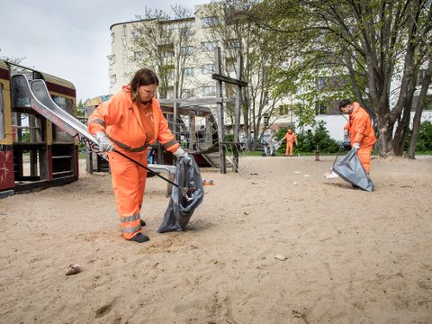 Spielplatzreinigung: Einsatzkräfte der BSR sammeln Abfall von einer Sandfläche (Bild: BSR / Stephan Pramme)