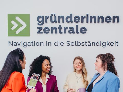 Vier Frauen reden und netzwerken vor dem Logo der Gründerinnenzentrale