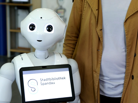 Ein Roboter mit einem Tablet auf der Brust mit der Aufschrift "Stadtbibliothek Spandau"