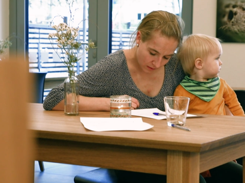 Eine Frau mit einem Kind auf dem Schoß liest etwas am Tisch
