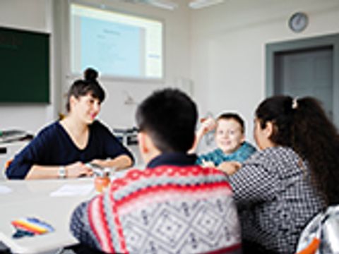 Eine Betreuerin und drei Kinder sitzen um einen Tisch.