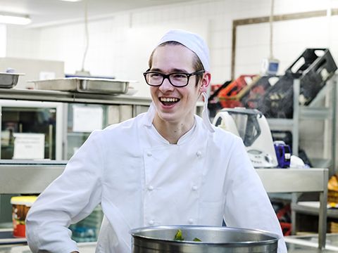 Ein junger Koch in Arbeitskleidung am Herd einer großen Küche