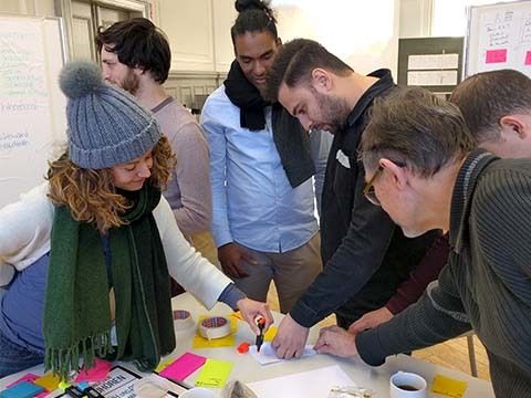 Mehrere Workshopteilnehmende an einem Tisch beschriften eine Moderationskarte