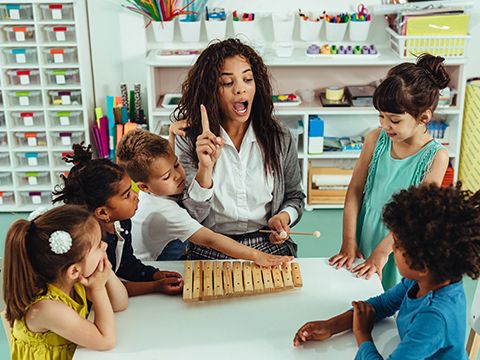 Eine Musiklehrerin umringt von Kindern hebt ihren rechten Zeigefinger