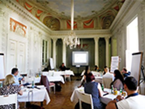 Menschen sitzen während einer Schulung an Tischen mit Blick auf eine Leinwand.