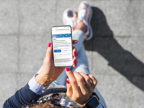 Frau hält ein Handy, auf dem Display ist das LinkedIn Profil der KEK zu sehen