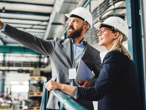Mann und Frau mit Helm in einer Fabrik