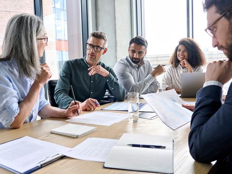 Fünf Menschen sitzen an einem Tisch und besprechen sich miteinander