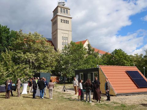 Eine Gruppe Menschen draußen, hinter Ihnen ein kleines Gebäude mit einem Solarpanel auf dem Dach.
