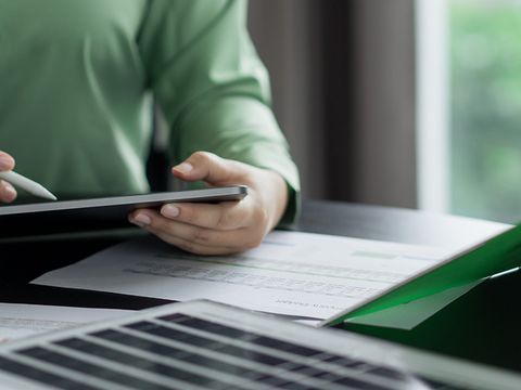 Nahaufnahme zwei Personen am Tisch, sitzend. Eine hält ein Tablet die Andere ein Klemmbrett mit Kugelschreiber. Vor ihnen liegt eine kleines Solarmodul.