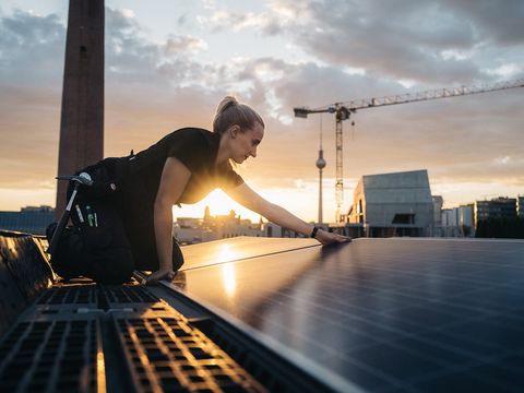 Frau bei der Installation eines Solarpanels. Im Hintergrund die Skyline von Berlin.