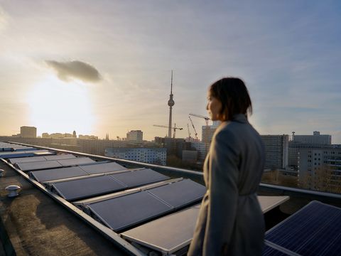 Eine Person auf einem Dach mit Solarpanelen. Im Hintergrund die Skyline von Berlin.