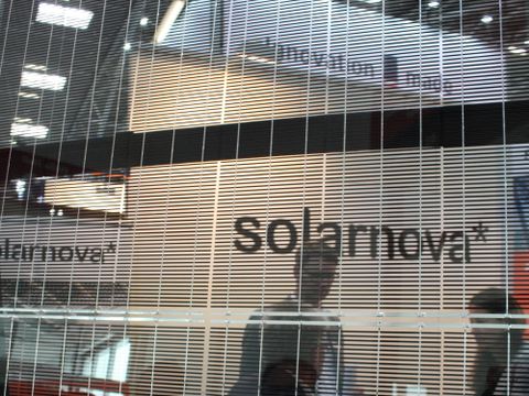 Bild eines semitransparenten Solarmoduls mit Siliziumlamellen durch das hindurch man Menschen auf einer Messe sieht.
