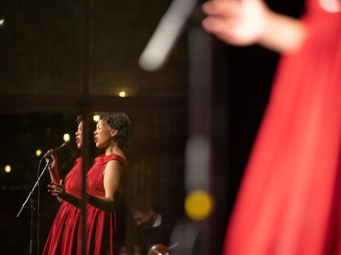In einem Spiegel ist eine Frau in rotem Kleid zu sehen, die mit einem MIkro singt
