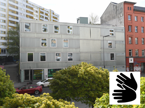 Fotografie der Mittelpunktbibliothek Wilhelm Liebknecht / Namik Kemal am Kottbusser Tor in Berlin Kreuzberg mit eingefügtem Gebärdensprachen-Logo